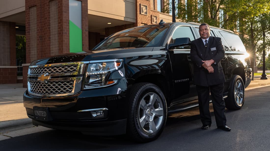 Uniformed chauffeur beside a black Suburban at golden hour